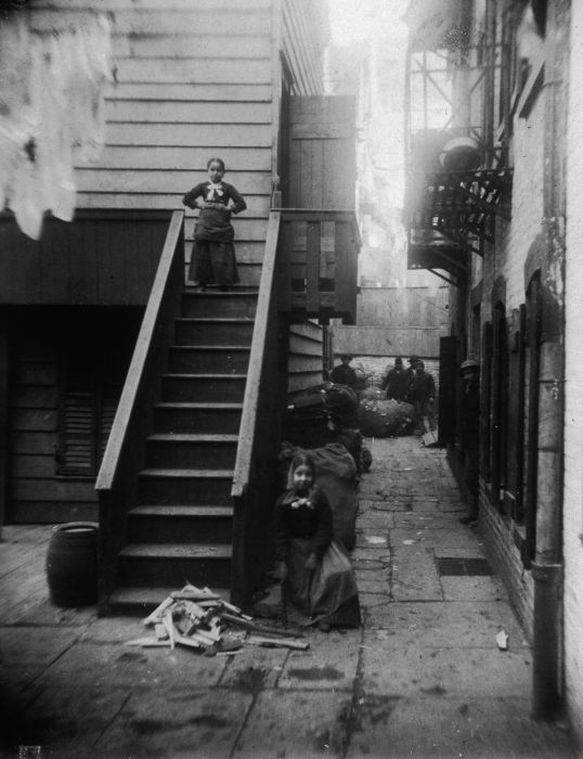 circa 1890: Two young girls, both ragpickers, stand at a staircase in Baxter Alley, Little Italy, New York City. The alley was known as 'Ragpickers Row.' (Photo by Jacob A. Riis/Museum of the City of New York/Getty Images)